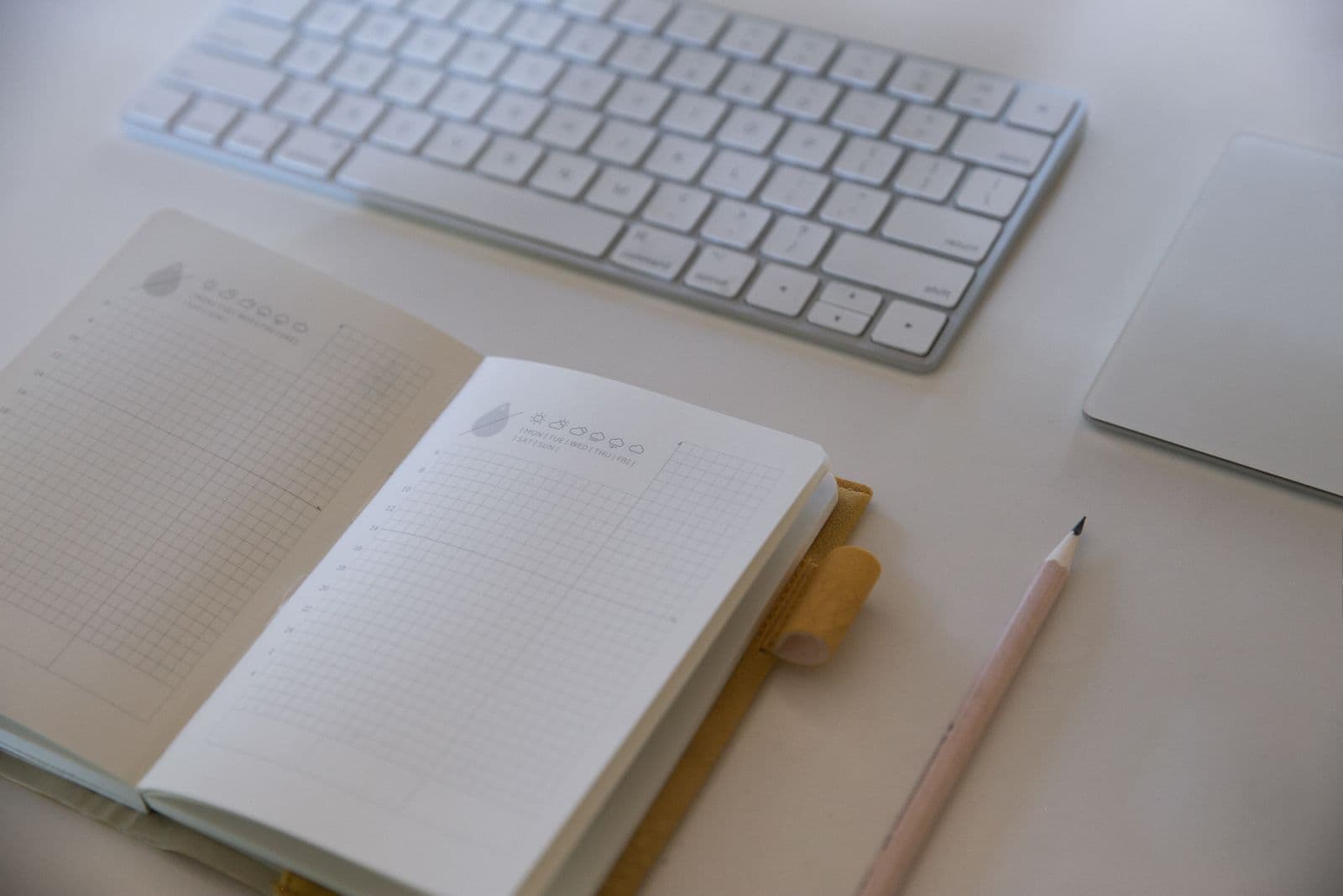 A tidy workspace with a keyboard, notebook and pencil arranged neatly