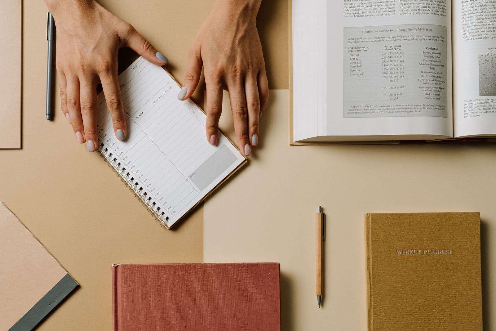 Hands arranging books and planners across a tidy working desk