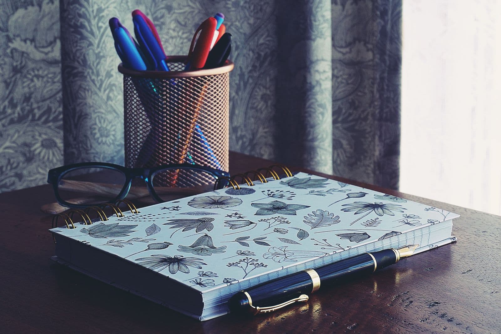 Reading glasses, a pen, and an open notebook on a wooden desk