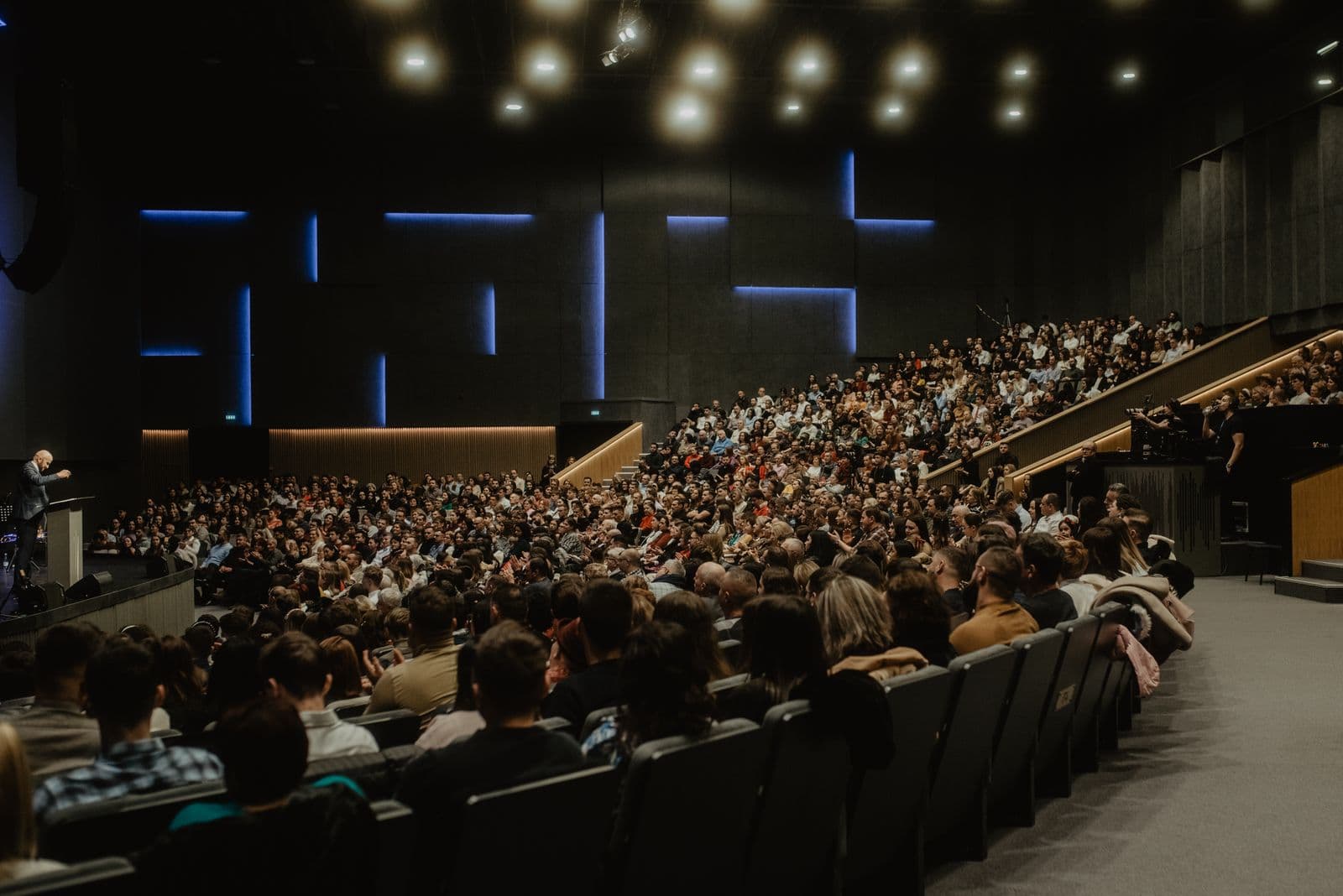 A large audience seated and listening to a presenter at an event